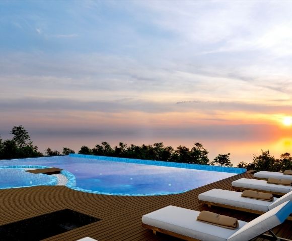 Rooftop infinity pool with sun loungers and ocean views during sunset, creating a relaxing resort atmosphere.