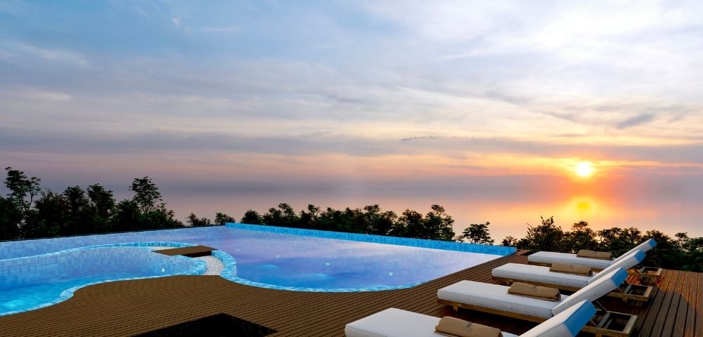Rooftop infinity pool with sun loungers and ocean views during sunset, creating a relaxing resort atmosphere.