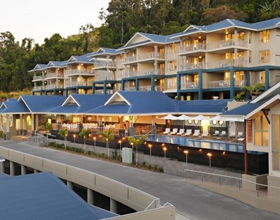 A modern resort complex with multiple levels of rooms and balconies, featuring blue roofs and a swimming pool area with lounge chairs.