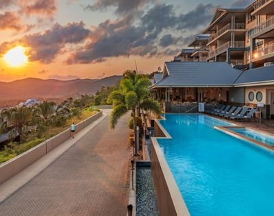 Resort pool with turquoise water, lounge chairs, and palm trees at sunset with mountains in the background.