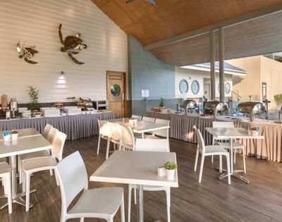 Buffet area with tables and chairs set up for dining, featuring chafing dishes, cereal dispensers, and decorative sea turtles on the wall.