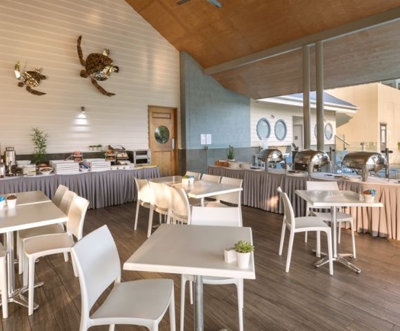 Buffet area with tables and chairs set up for dining, featuring chafing dishes, cereal dispensers, and decorative sea turtles on the wall.