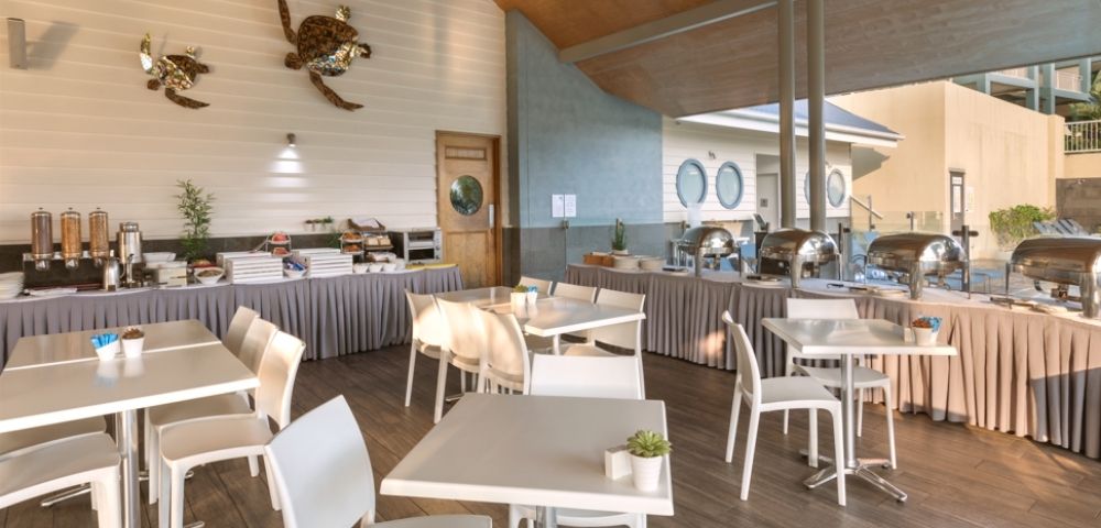 Buffet area with tables and chairs set up for dining, featuring chafing dishes, cereal dispensers, and decorative sea turtles on the wall.