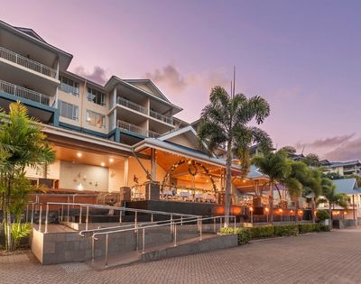 A multi-story resort building with balconies and palm trees, illuminated by warm lighting in the evening.