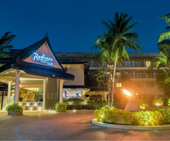 Radisson Resort & Suites Phuket entrance at dusk with tropical palm trees and a lit torch.