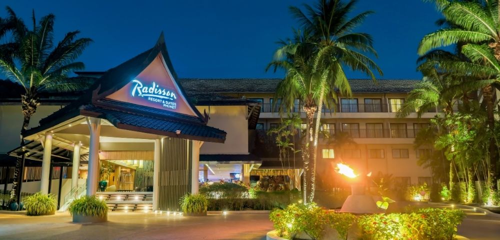 Radisson Resort & Suites Phuket entrance at dusk with tropical palm trees and a lit torch.