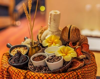 Spa treatment arrangement with coffee beans, cocoa powder, dried fruit slices, and a herbal compress ball.