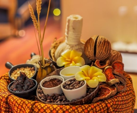 Spa treatment arrangement with coffee beans, cocoa powder, dried fruit slices, and a herbal compress ball.