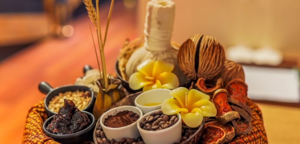 Spa treatment arrangement with coffee beans, cocoa powder, dried fruit slices, and a herbal compress ball.