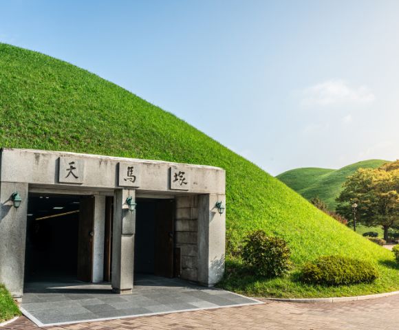 Entrance to a large, grassy tumulus with two archways and stone inscriptions under a bright blue sky.