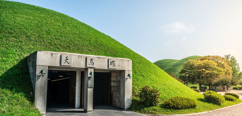 Entrance to a large, grassy tumulus with two archways and stone inscriptions under a bright blue sky.