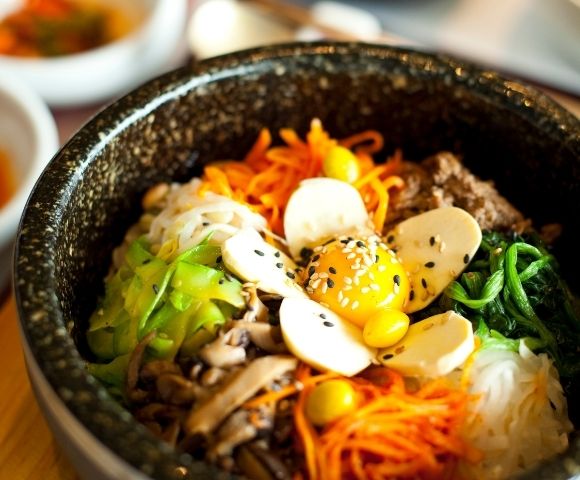 A close-up of a bibimbap bowl with assorted vegetables, sliced mushrooms, raw egg yolk, and sesame seeds on top.