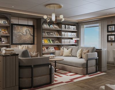A cozy library lounge with bookshelves filled with books and magazines, comfortable sofas, armchairs, a small coffee table, and a framed map on the wall, bathed in soft light.