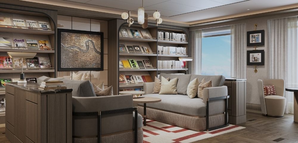 A cozy library lounge with bookshelves filled with books and magazines, comfortable sofas, armchairs, a small coffee table, and a framed map on the wall, bathed in soft light.