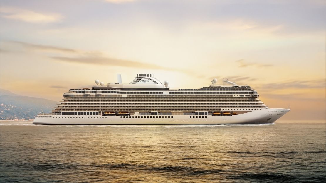 A large, modern white cruise ship sailing on calm ocean water with a golden sky and distant mountains.