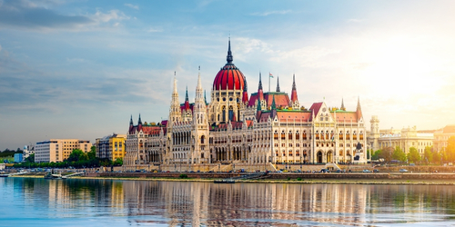 Hungarian Parliament Building with its detailed Gothic Revival architecture reflecting on the calm Danube River under a clear sky.