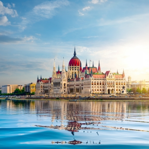 Hungarian Parliament Building with its detailed Gothic Revival architecture reflecting on the calm Danube River under a clear sky.