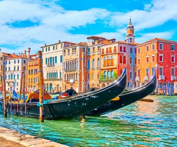 Two black gondolas docked on a canal with colorful historic buildings and a blue sky in the background, Venice, Italy.