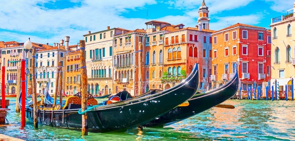 Two black gondolas docked on a canal with colorful historic buildings and a blue sky in the background, Venice, Italy.