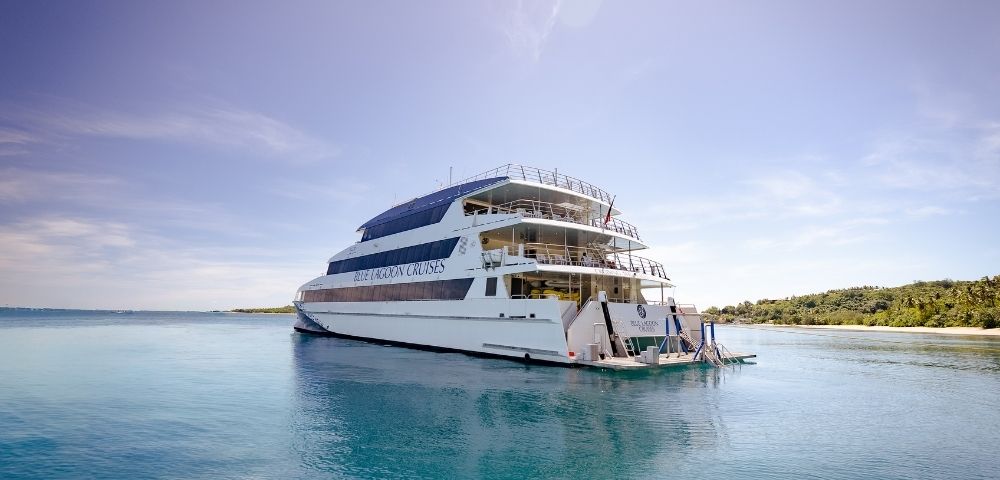 A large cruise ship anchored in calm, turquoise waters with a clear blue sky and a green island in the background.