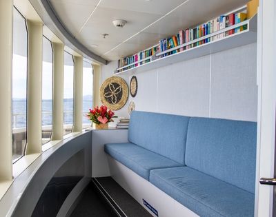 A cozy seating area with a blue couch, bookshelves filled with books, and decorative items by large windows overlooking the ocean.