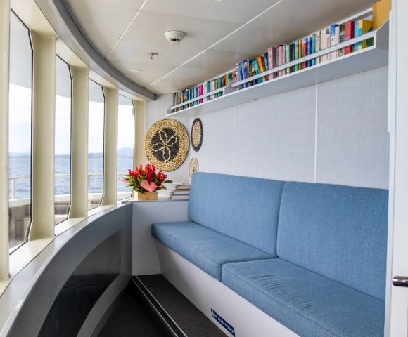 A cozy seating area with a blue couch, bookshelves filled with books, and decorative items by large windows overlooking the ocean.