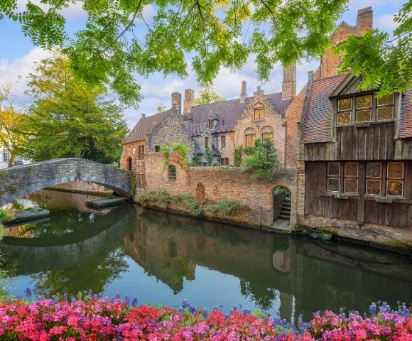 A stone bridge arches over a tranquil canal reflecting historic brick buildings and trees.