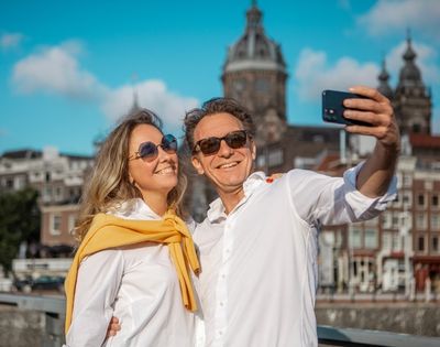 A smiling couple takes a selfie with a city skyline in the background.
