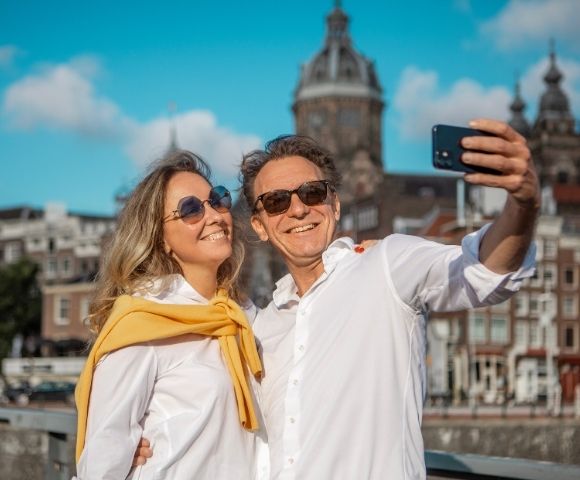 A smiling couple takes a selfie with a city skyline in the background.