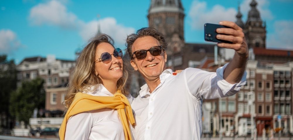 A smiling couple takes a selfie with a city skyline in the background.