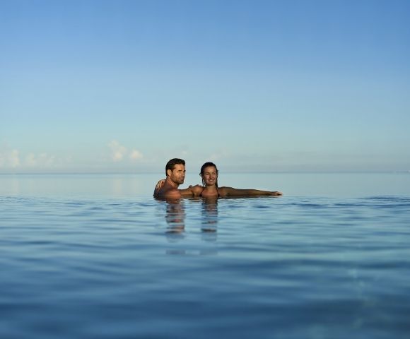 A couple enjoying a peaceful moment in a calm body of water, with clear blue skies above.