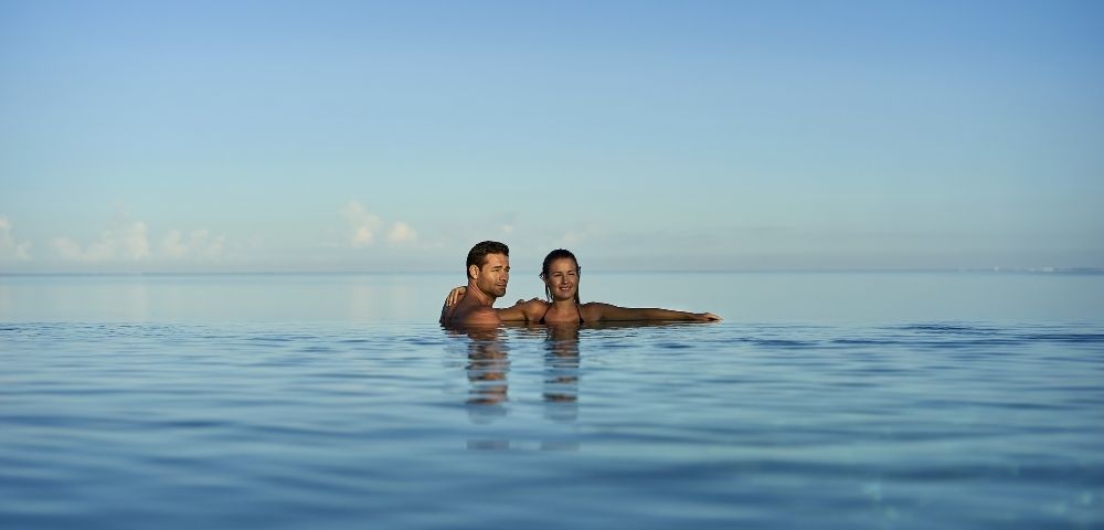 A couple enjoying a peaceful moment in a calm body of water, with clear blue skies above.
