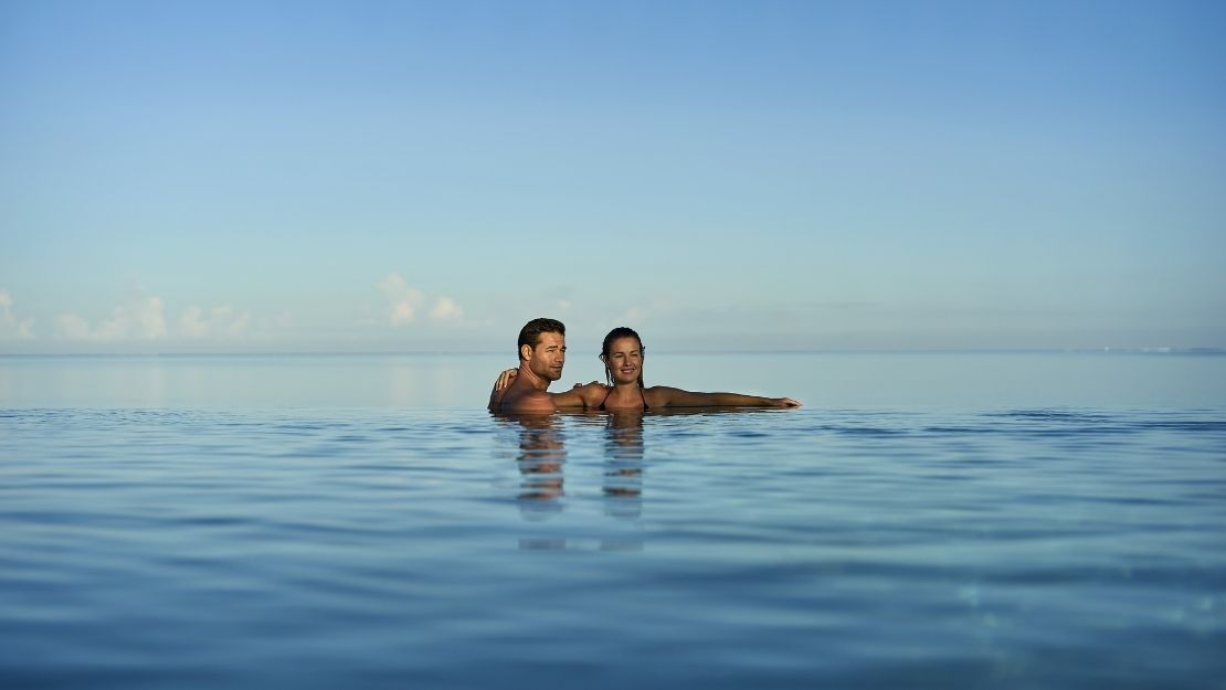 A couple enjoying a peaceful moment in a calm body of water, with clear blue skies above.