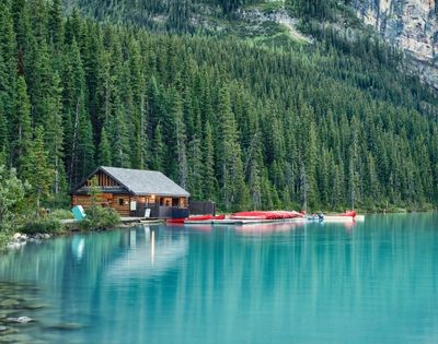A serene lake surrounded by tall evergreen trees, featuring a wooden cabin and colorful canoes lined up at the water's edge.