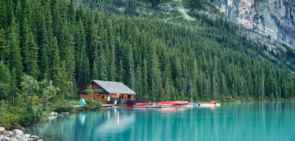 A serene lake surrounded by tall evergreen trees, featuring a wooden cabin and colorful canoes lined up at the water's edge.