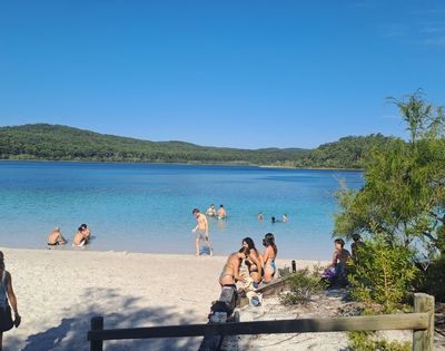 A beach scene with people swimming and relaxing near clear blue water and green hills in the background.