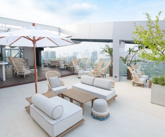 A rooftop lounge area featuring comfortable seating, umbrellas, and a view of the city skyline.