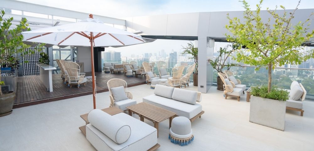 A rooftop lounge area featuring comfortable seating, umbrellas, and a view of the city skyline.