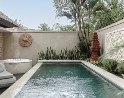 A serene backyard with a small swimming pool, a hot tub, lush greenery, and decorative stone walls.