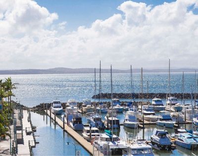 A scenic view of a marina with numerous boats and yachts docked, set against a shimmering body of water and a partly cloudy sky.