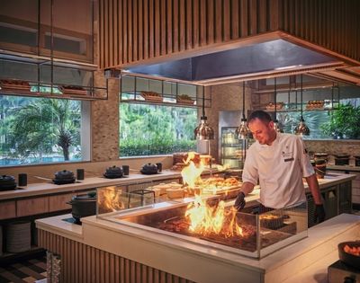 A chef expertly manages a grill with flames in a modern kitchen setting.