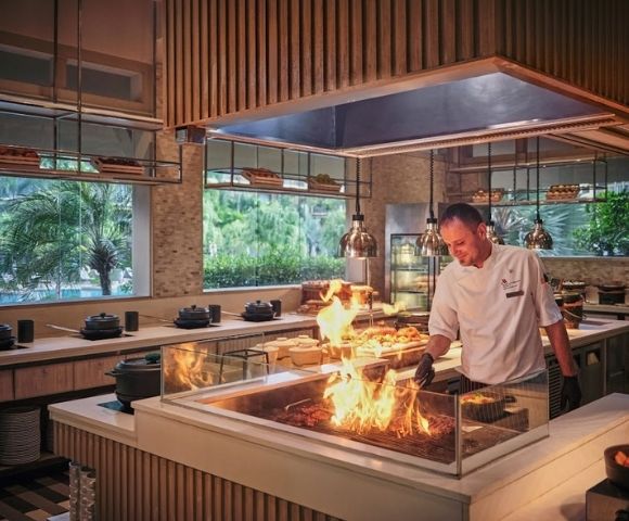 A chef expertly manages a grill with flames in a modern kitchen setting.