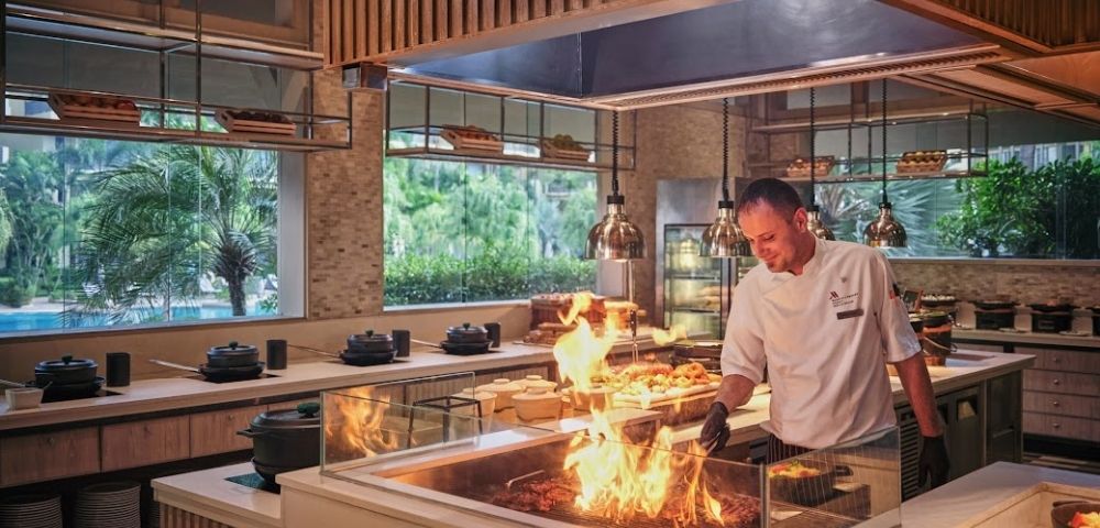 A chef expertly manages a grill with flames in a modern kitchen setting.