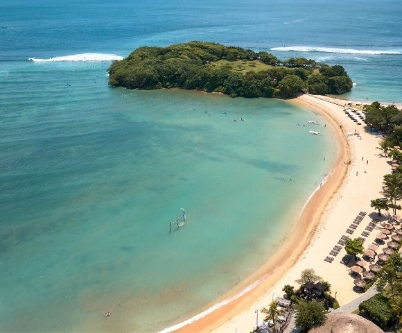 Aerial view of a beach with clear water, an island in the distance, and people enjoying the shoreline.