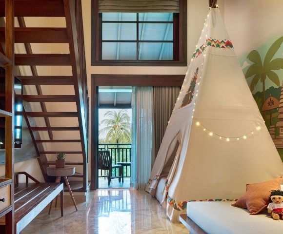 A cozy room featuring a staircase, a tent structure, and tropical-themed decor with dolls on a bed.