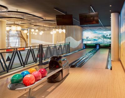 A modern bowling alley featuring multiple lanes, colorful bowling balls on a rack, and decorative murals on the walls.