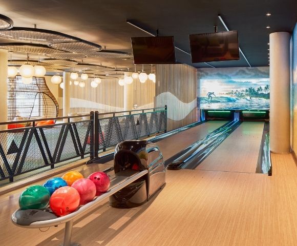 A modern bowling alley featuring multiple lanes, colorful bowling balls on a rack, and decorative murals on the walls.