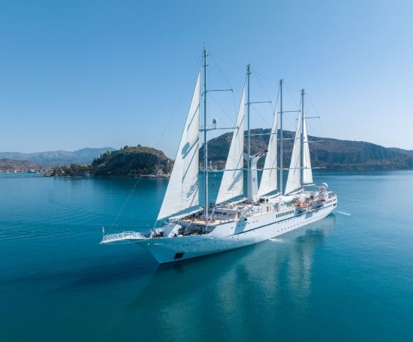 White sailing yacht anchored in a tranquil bay with mountains in the distance.
