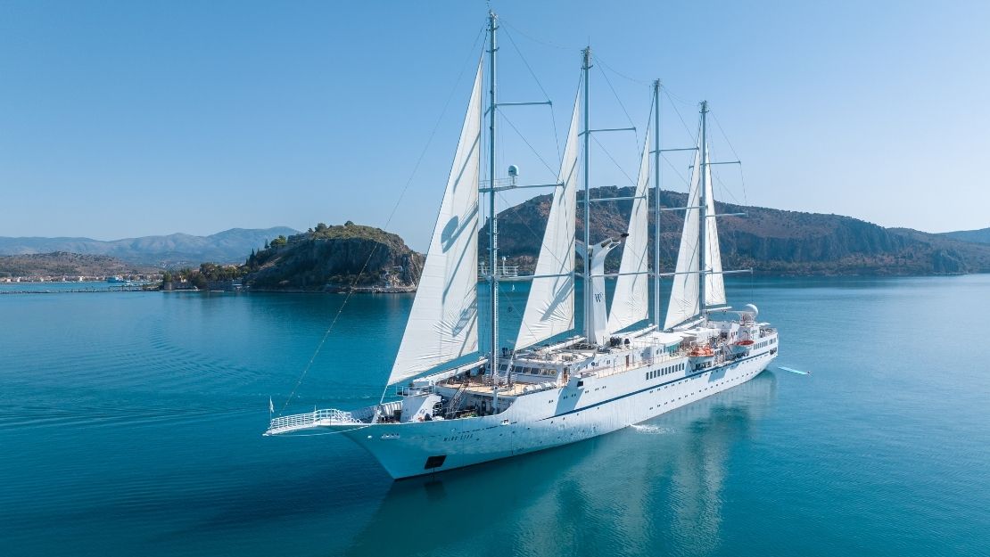 White sailing yacht anchored in a tranquil bay with mountains in the distance.