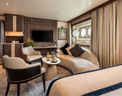 Spacious cruise ship suite with seating area, large windows, and modern furnishings.